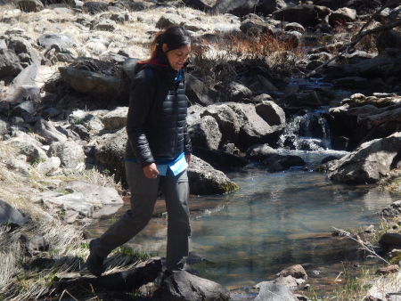 Ruth crossing a river on the way to Hell Canyon with a waterfall in the background
