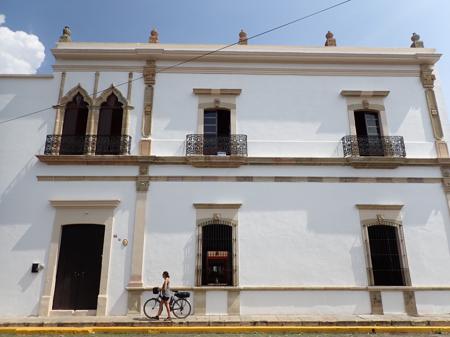Ruth walking on the pavement with a white colonia building behind her