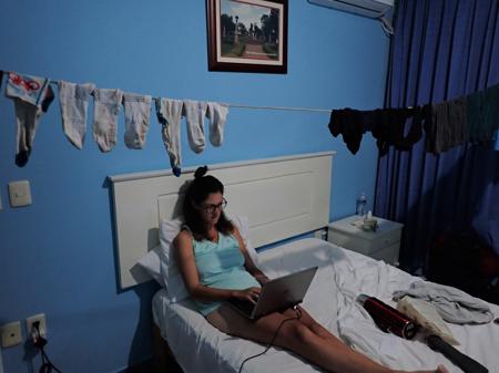 Ruth in bed writing the blog with clothing hanging in the middle of the room