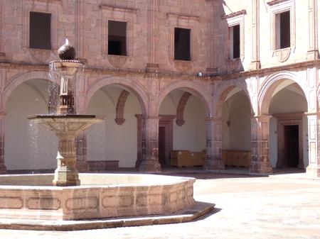 A fountain glistening in the sun at the centre of a plain courtyard