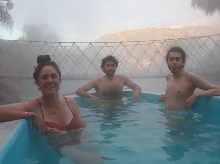 Ruth, Gus and Oscar in a hot spring with a rope bridge in the background