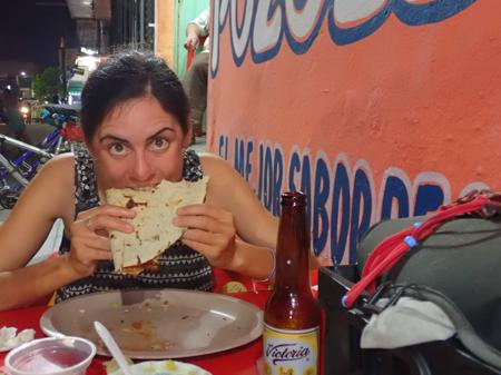 Ruth eating a tlayuda with a beer out in the outdoor seating of a bar